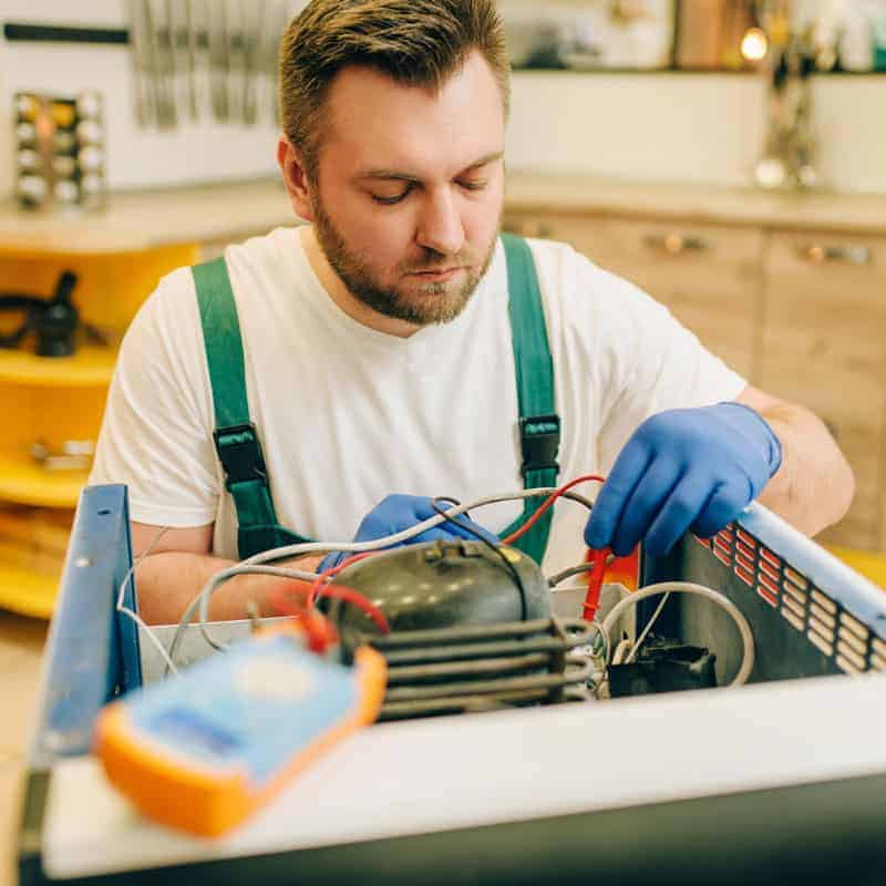 Professional appliance repair technician diagnosing equipment with test tools